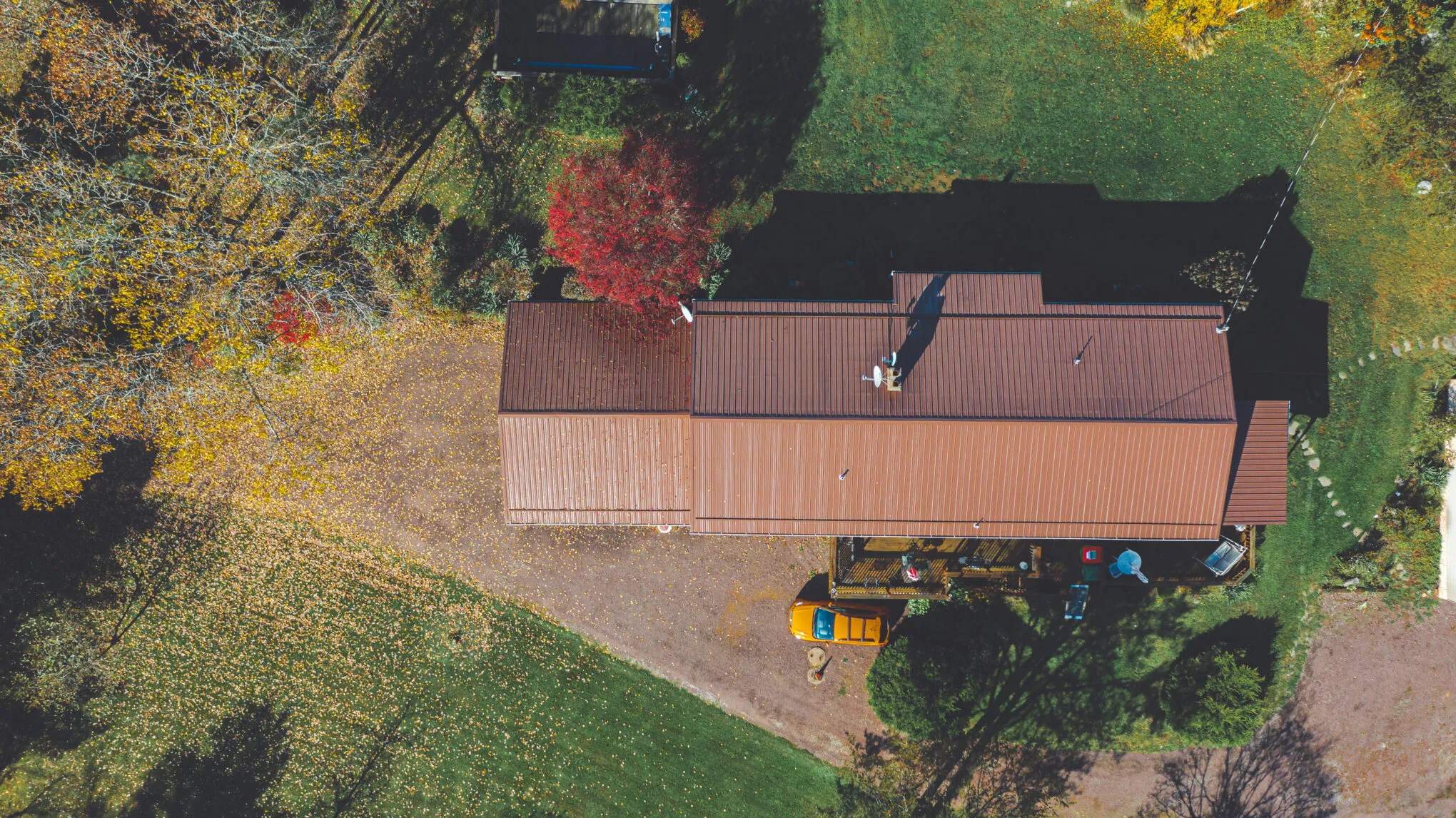 Overhead drone view of a long building with a new brown metal roof, ringed by autumn trees on a Pennsylvania property