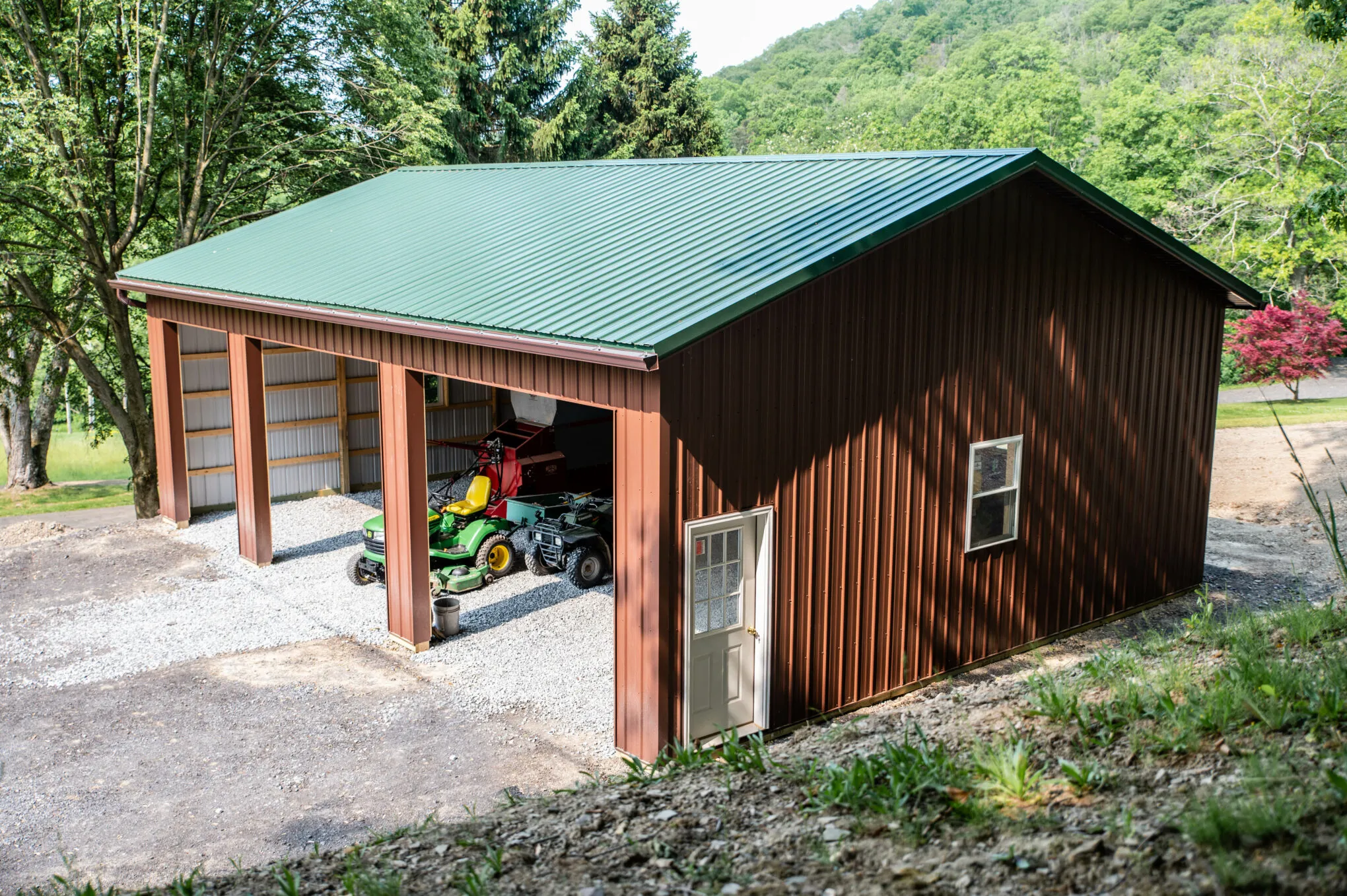 A brown post-frame building with a green metal roof set against a wooded Pennsylvania hillside