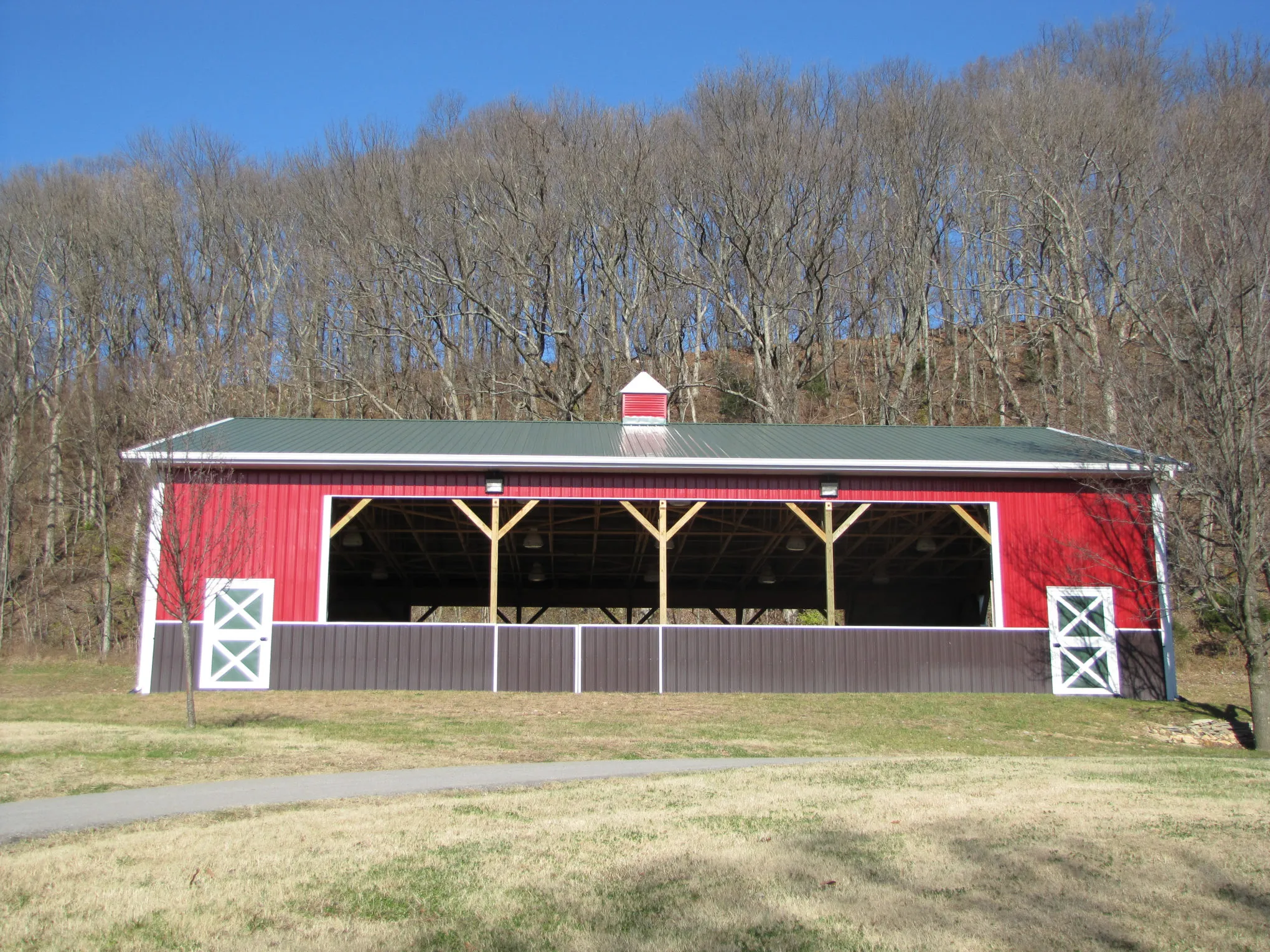 Bright red open-front pavilion with a green metal roof, white trim, and exposed wooden posts and trusses across the open side